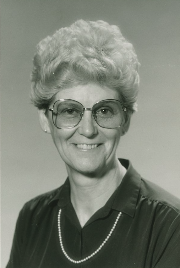 A black and white photo of someone smiling wearing big glasses, a collar and a necklace